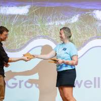 Teacher receives hug from Groundswell staff in a blue T-shirt in front of projected "Groundswell" background